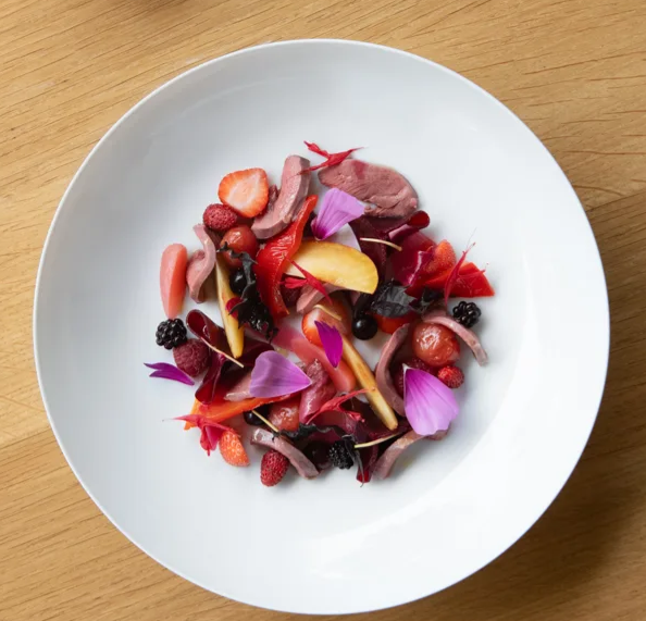 Assiette de salade avec des fruits, de la viande, des pétales de fleurs et des baies, vue du dessus.