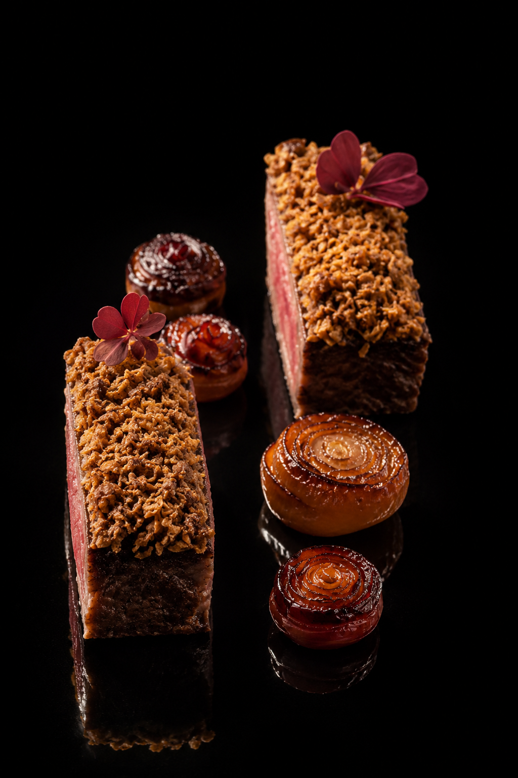 Deux entremets rectangulars recouverts de crumble, décorés de petites fleurs rouges, accompagnés de cerises grillées en spirale sur un fond noir.
