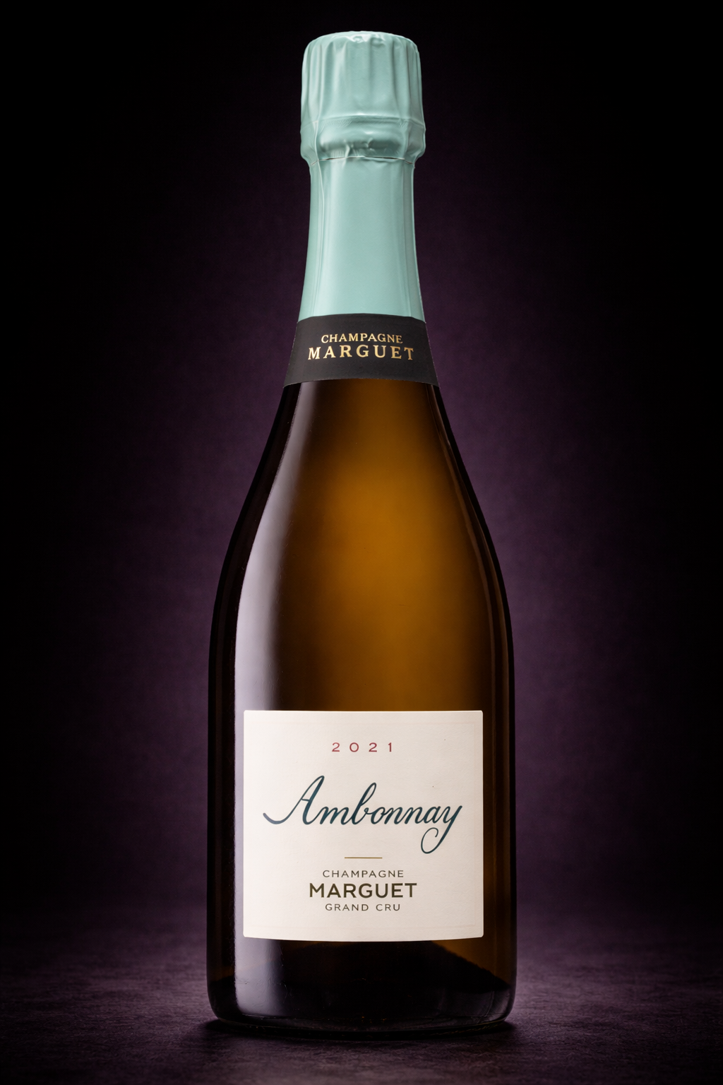 Bouteille de champagne Marguet Ambonnay 2021, avec un étiquette blanche et un col en papier turquoise, sur un fond noir.