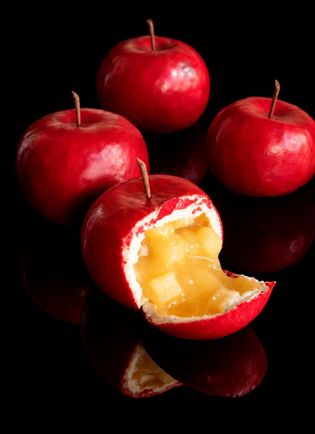Quatre pommes rouges avec un intérieur de crème et de fruits en gelée, sur un fond noir.