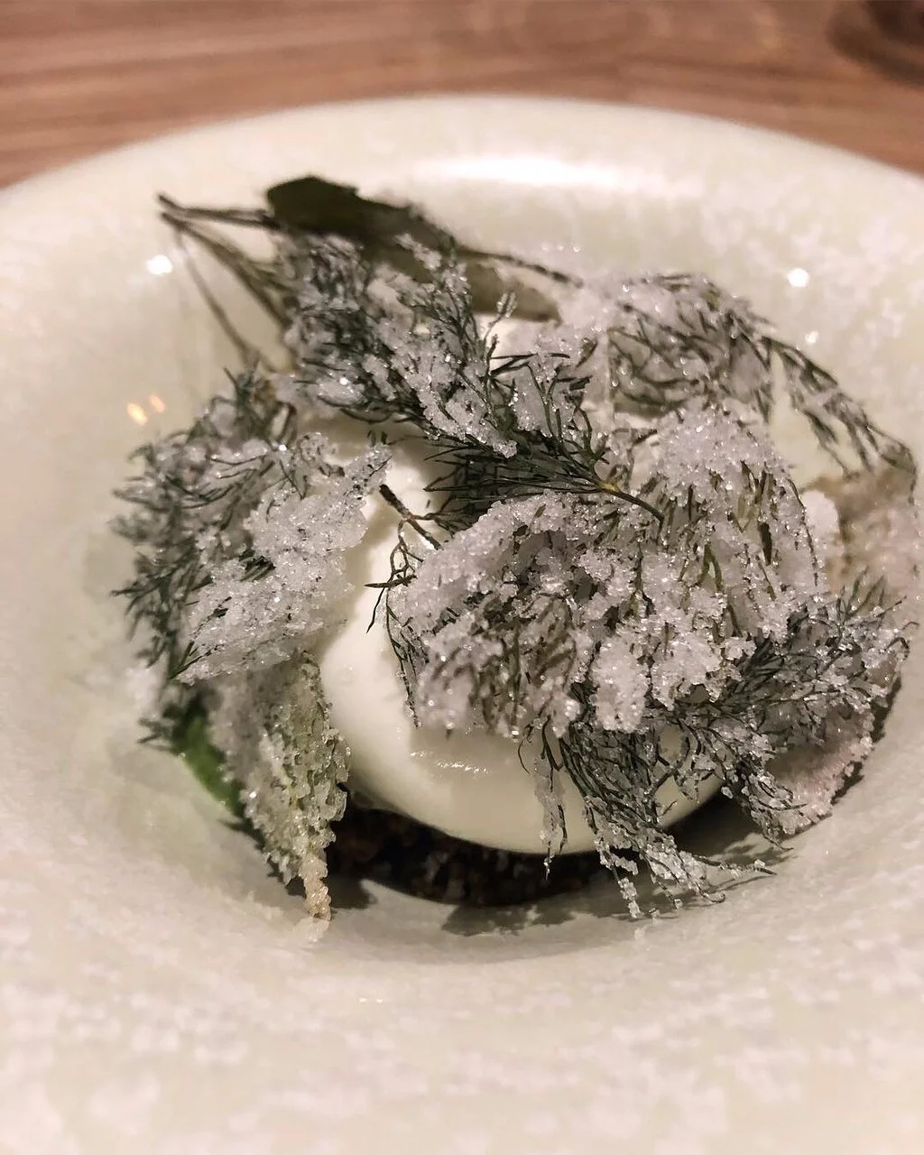 Dessert avec feuilles de fenouil gelées, crème et poudre blanche par-dessus.
