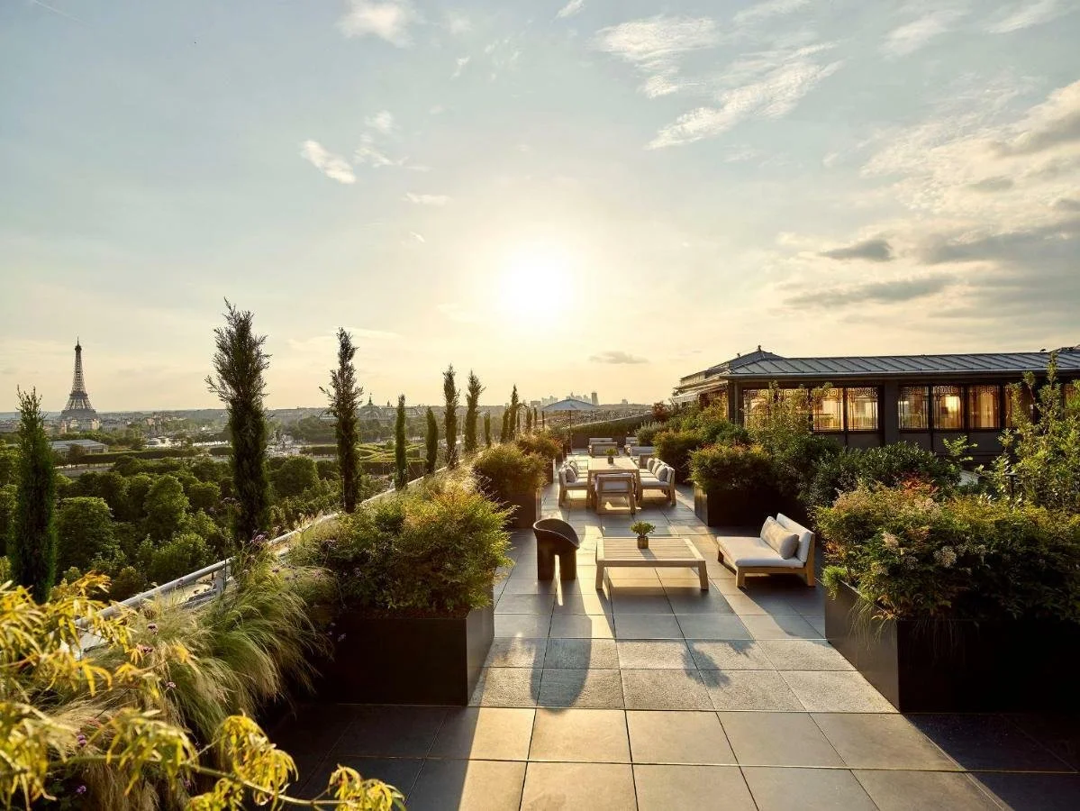 Terrasse en hauteur avec mobilier de salon, plantes en pot, vue sur la tour Eiffel au coucher du soleil, à Paris.