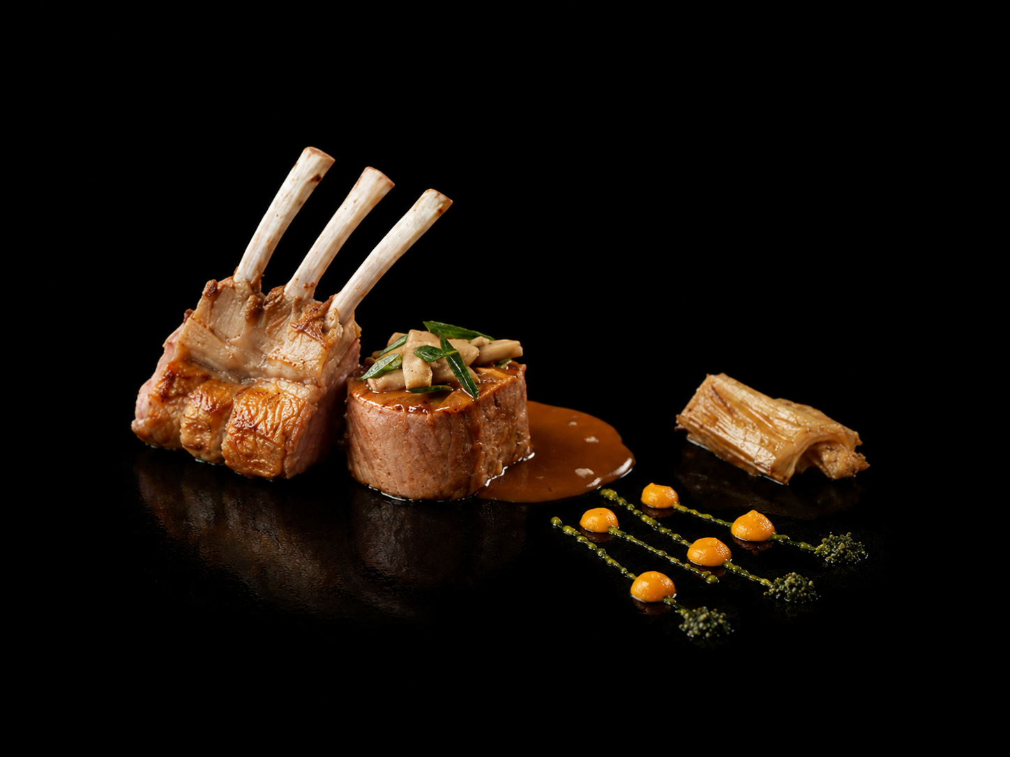 Assiette avec un gigot d'agneau rôti, une rondelle de filet mignon avec une sauce et garniture, une tranche de plein, décorations culinaires avec des sauces et des herbes, sur fond noir.