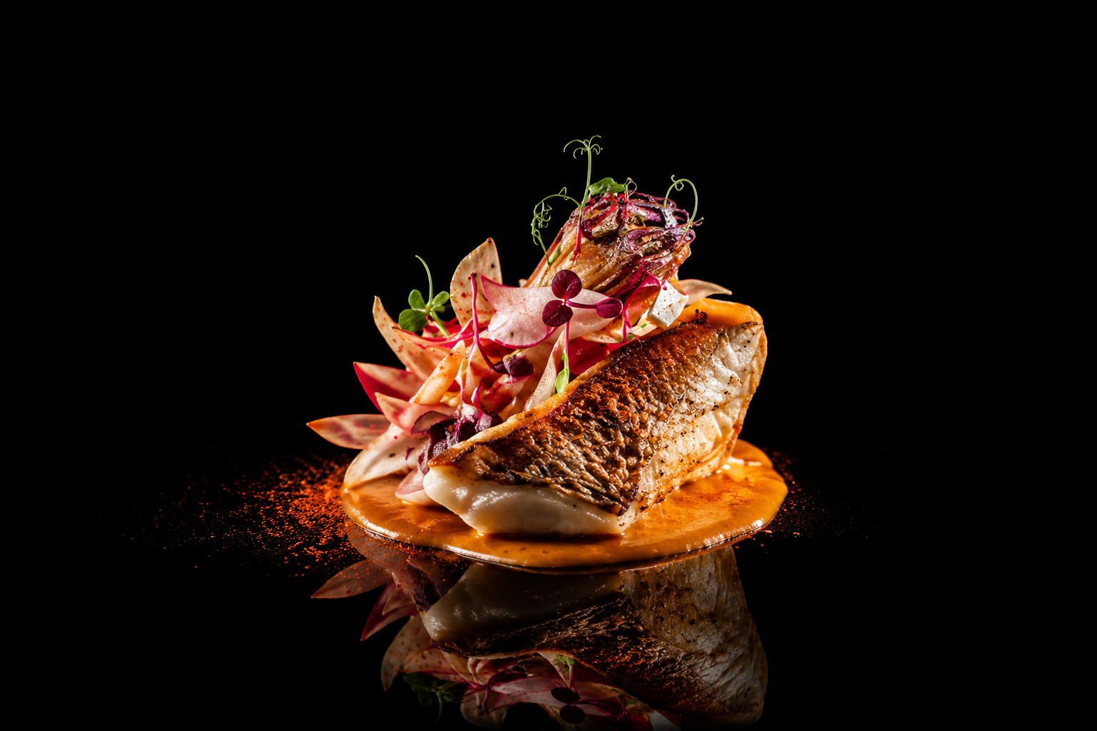 Assiette de poisson avec légumes colorés et garnitures, présentée sur une surface noire avec reflet.