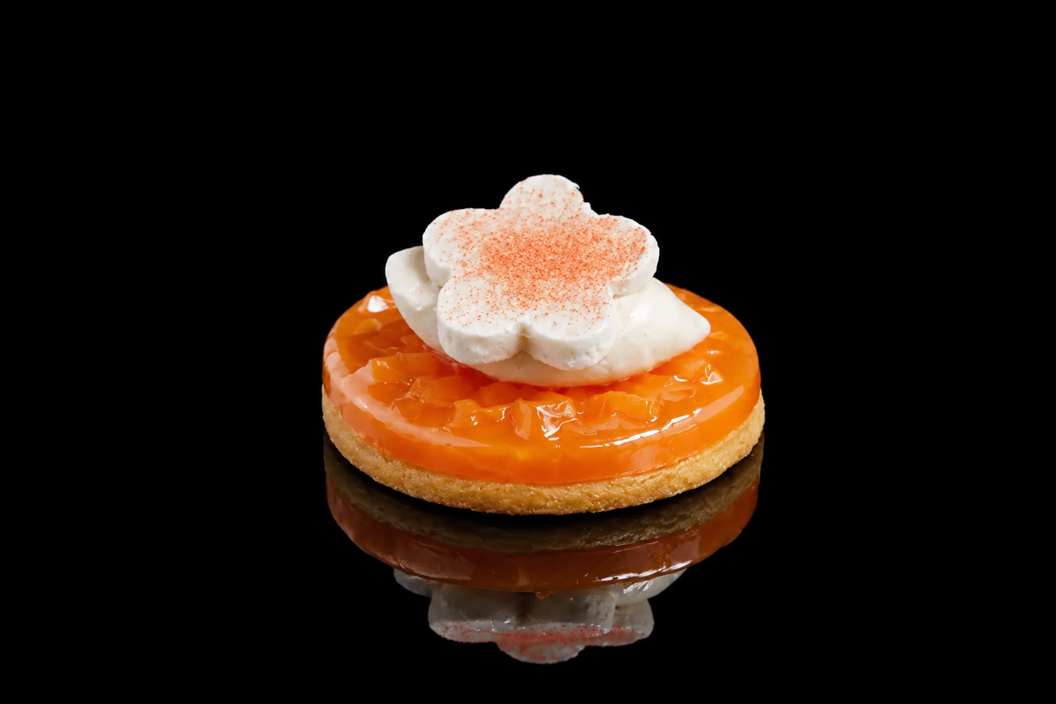 Petit biscuit garni de tranche d'orange, crème fouettée en forme de fleur, dusting de cannelle, sur fond noir.