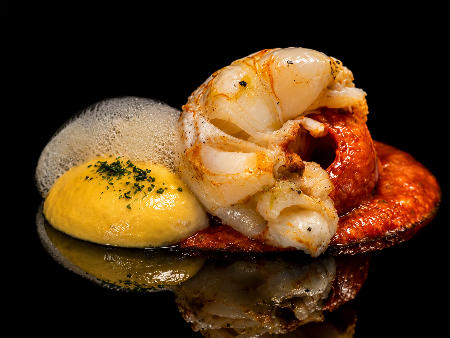 Gambas, œuf miroir avec mousse, sauce rouge sur une surface noire