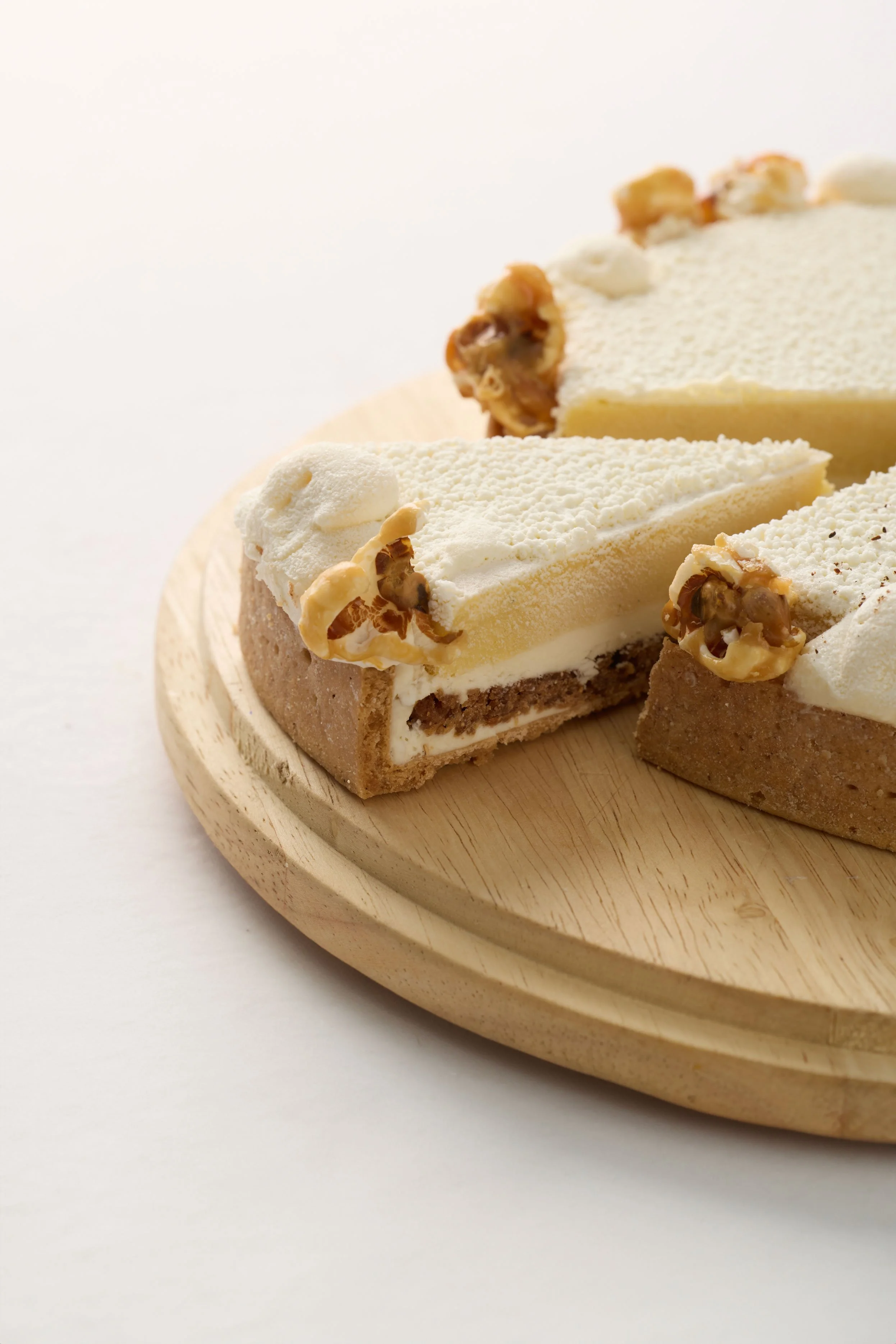 Gâteau sur une planche en bois, avec une tranche coupée montrant une base de biscuit, une couche de crème et des noix garnissant le dessus.