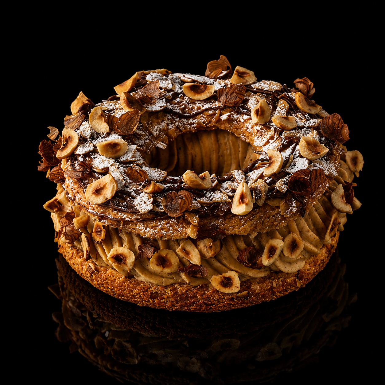 Gâteau rond décoré de noisettes, de chocolat fondu, saupoudré de sucre glace, avec une base de pâte croustillante, contre un fond noir.