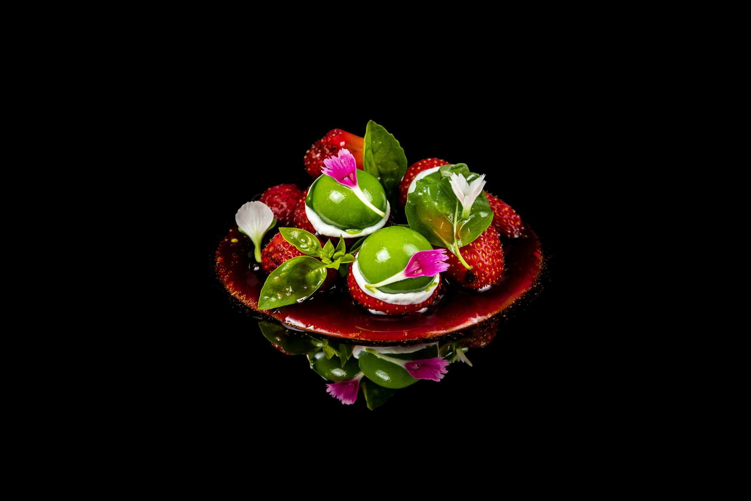 Plate de desserts avec des spheres vertes, fraises, feuilles et fleurs roses et blanches, sur fond noir