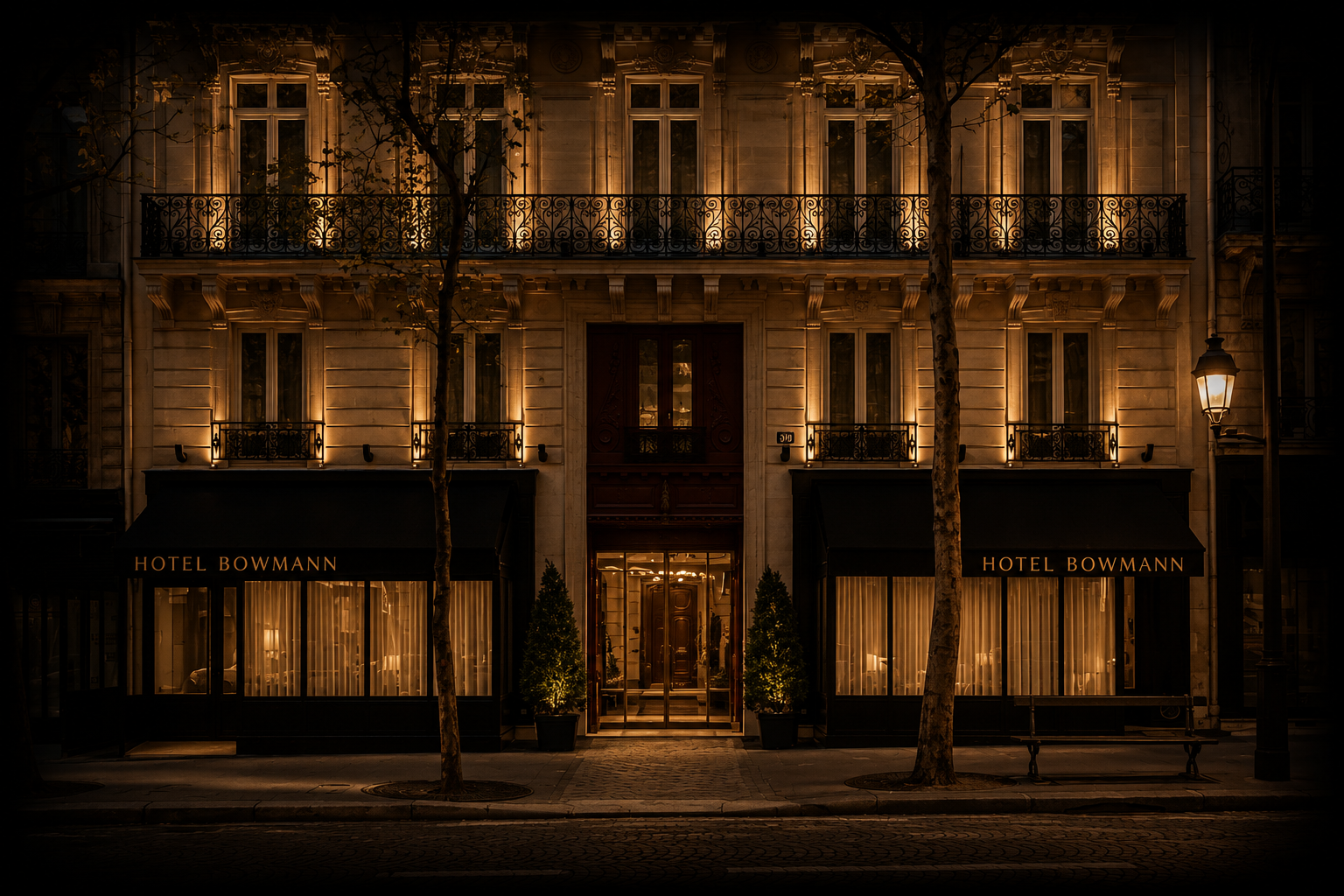 Façade éclairée de l'hôtel Bowmann la nuit, avec deux grands arbres en avant et des fenêtres illuminées.