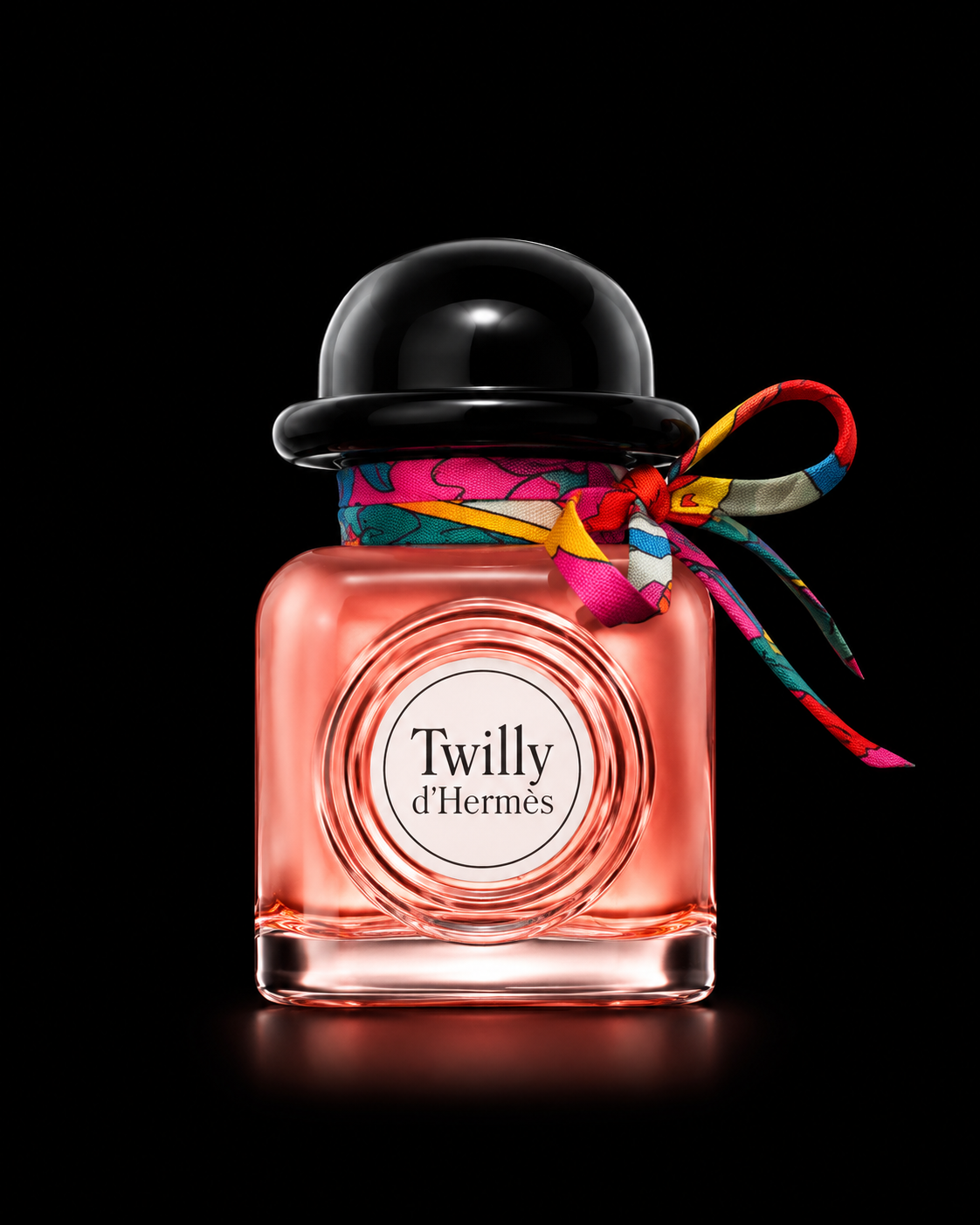 Parfum Twilly d'Hermès dans un flacon en verre rose, avec un bouchon noir, décoré d'un foulard coloré noué autour du col, sur un fond noir.