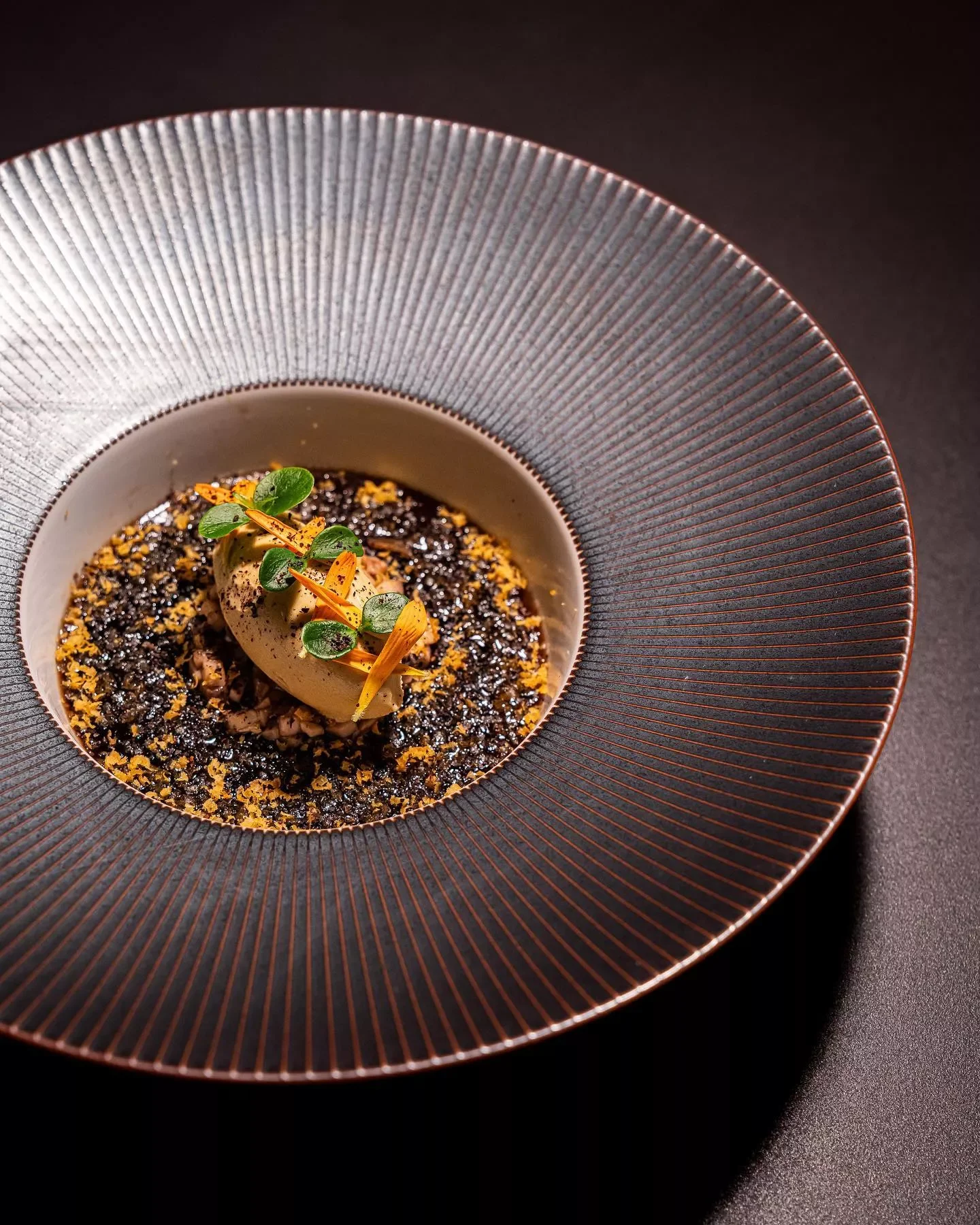 Dessert avec crème, garniture verte, pépites de chocolat ou d'épices, présenté dans un bol blanc dans une grande assiette noire à rayures.
