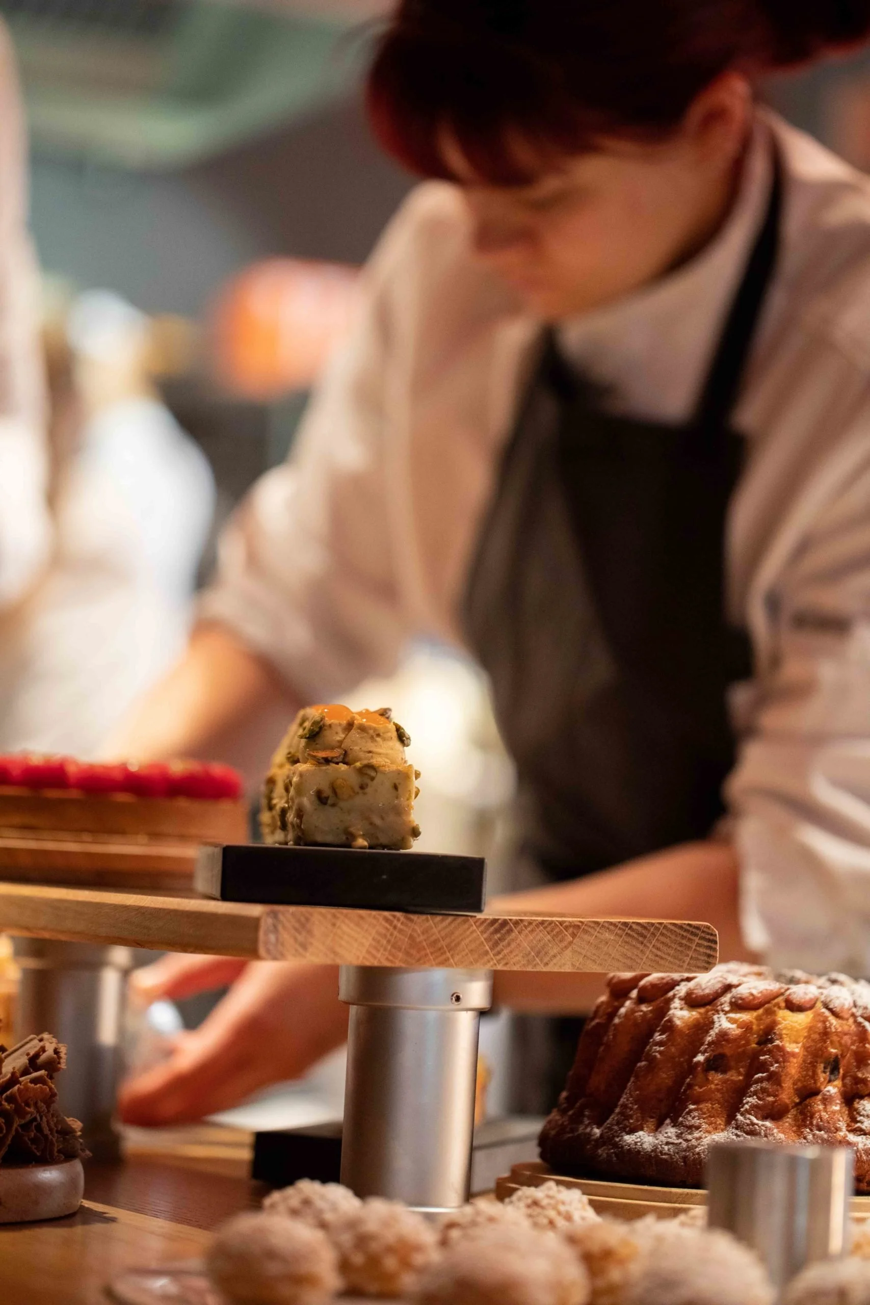 Un pâtissier en arrièregard, travaillant derrière un comptoir de pâtisseries, avec un gâteau moelleux en premier plan.