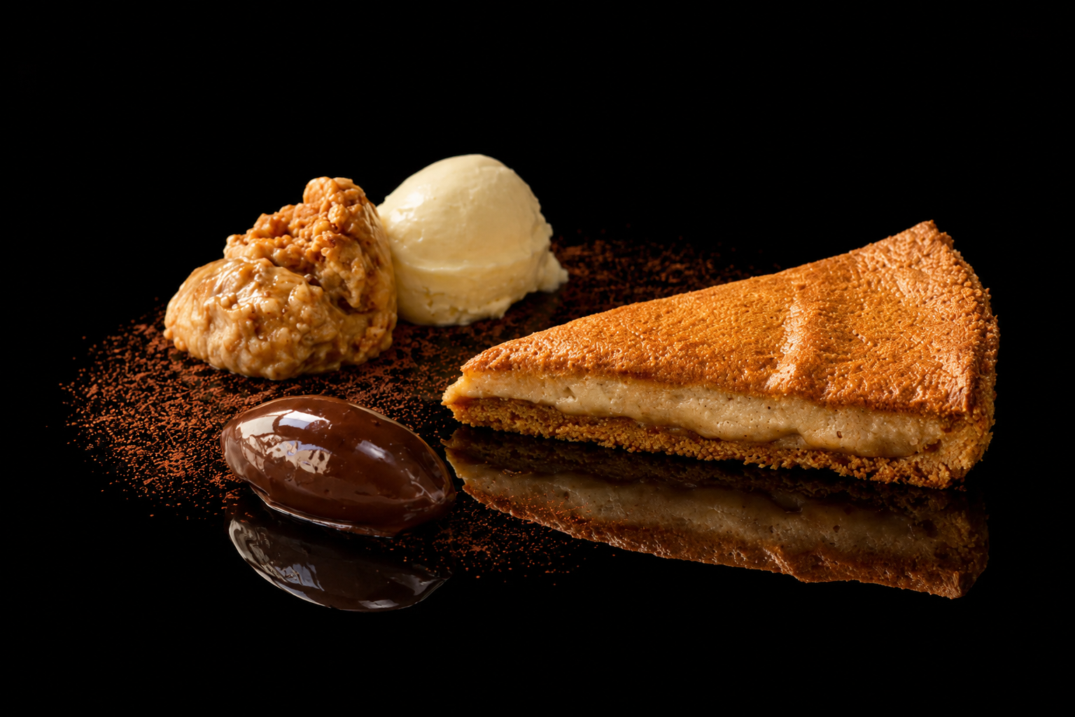Une tarte aux pommes avec glace à la vanille, une boule de crème glacée à la vanille, une quenelle de chocolat et des morceaux de caramel, présentés sur un fond noir avec un effet miroir.