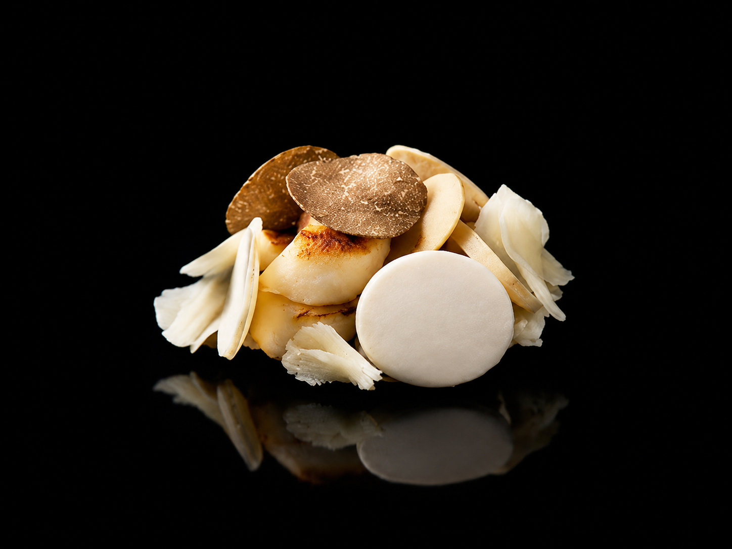 Petite pile de gommes de mascarpone garnies de copeaux de chocolat blanc et noir, placée sur fond noir avec reflet sous la pâte.