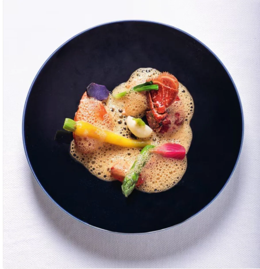Assiette de fruits de mer avec espuma et légumes colorés, présentée dans un bol noir.