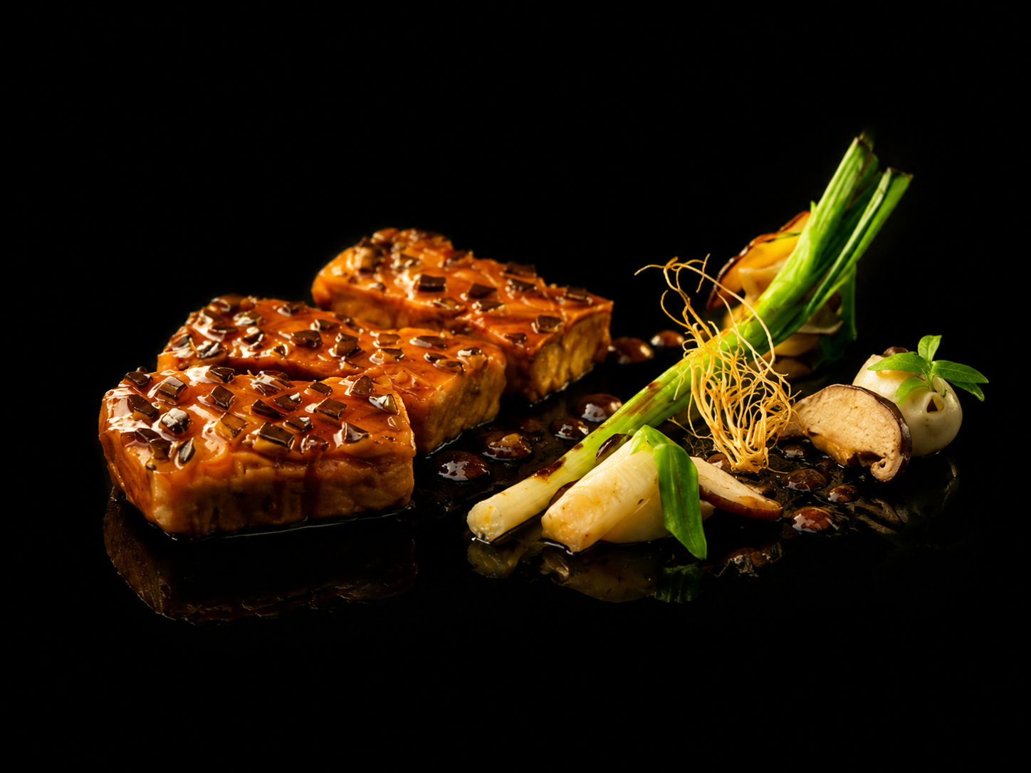 Gourmet plat avec trois morceaux de viande recouverts de sauce et de petits morceaux de légumes, accompagné de légumes verts, champignons, oignons de printemps, jeunes pousses et un petit piment, présentation élégante sur fond noir.