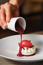 Un chef verse un coulis de fruit rouge sur une boule de glace à la vanille