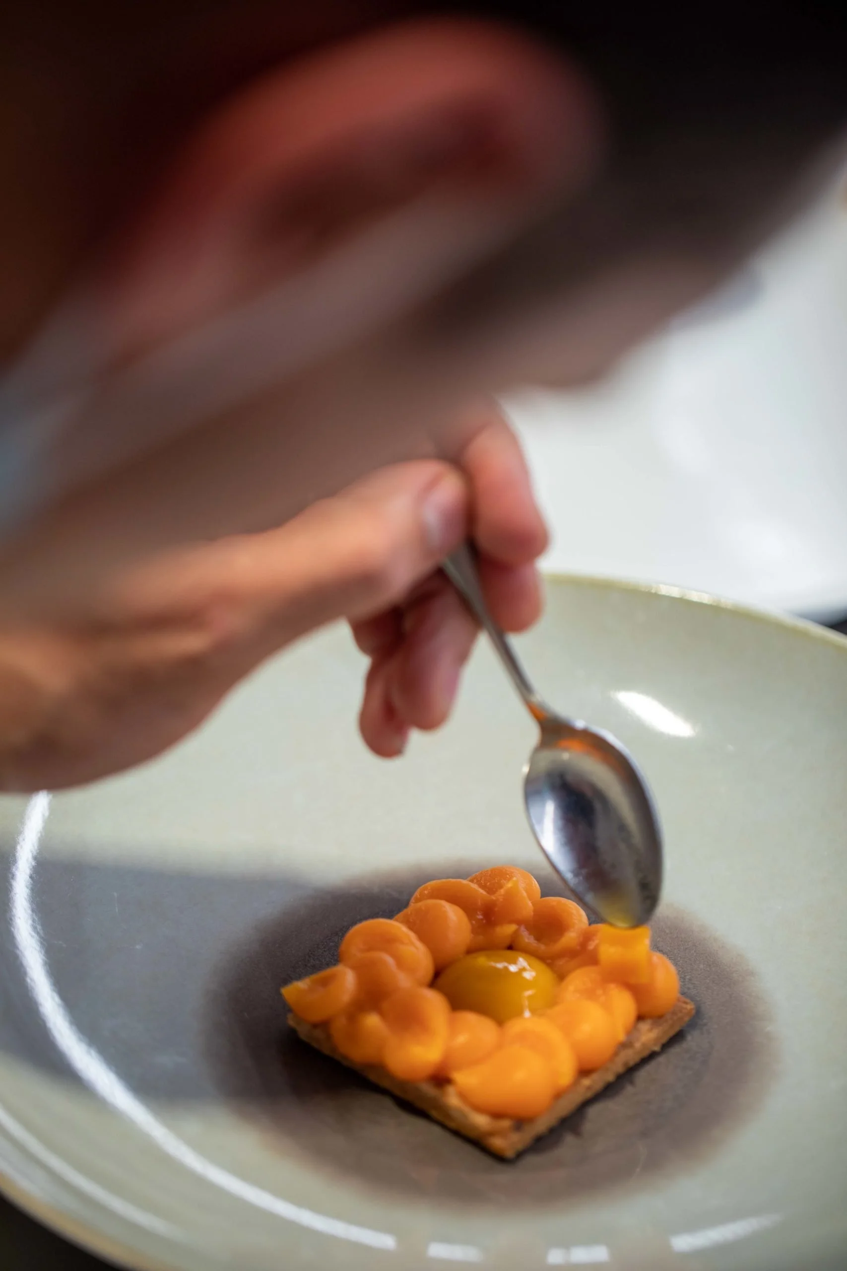 Une personne ajoute une cuillerée de confiture d'abricots sur une tranche de pain ou de biscuit à l'aide d'une cuillère.