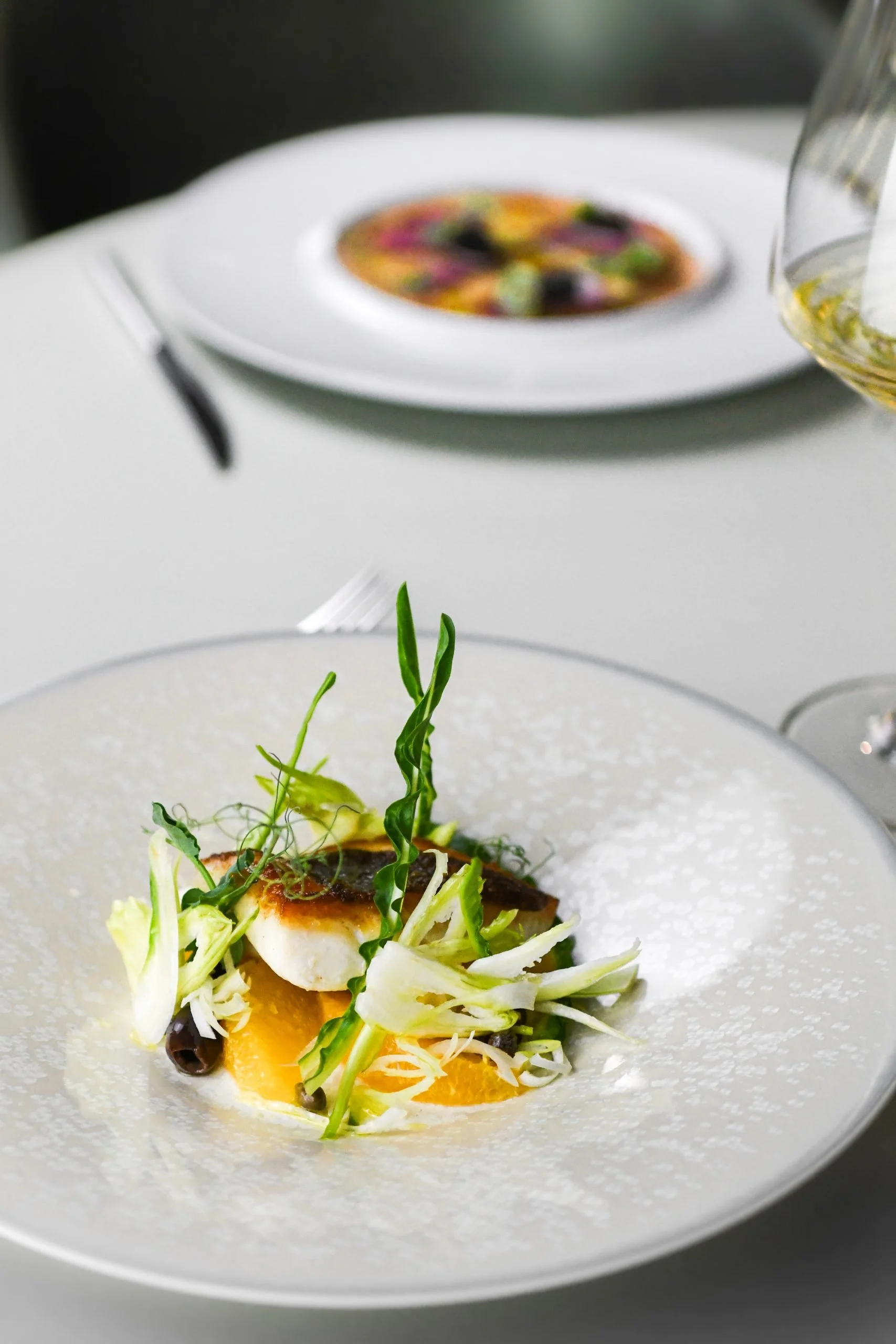 Assiette gastronomique avec un plat de poisson, légumes et sauce, présentation élégante, dans un cadre sophistiqué.