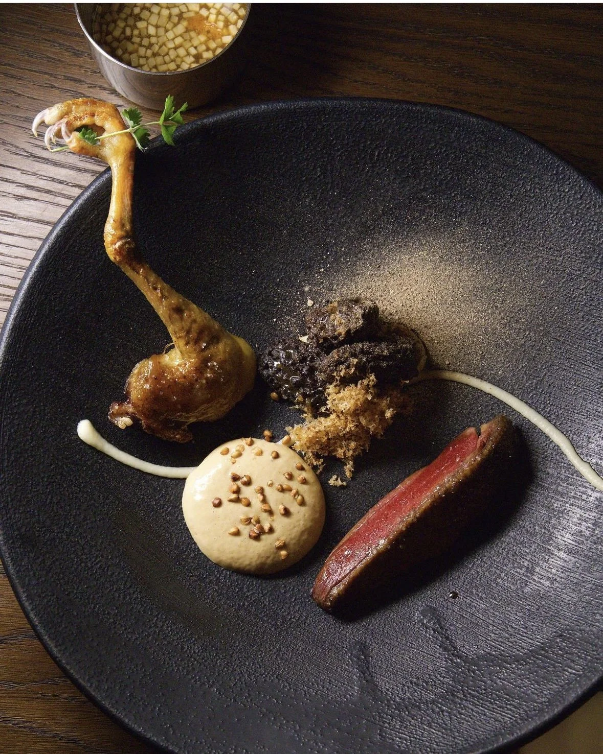Assiette minimaliste avec un cuisse de poulet farcie, un morceau de steak rouge, une quenelle de sauce, et des garnitures de croustille et de crème