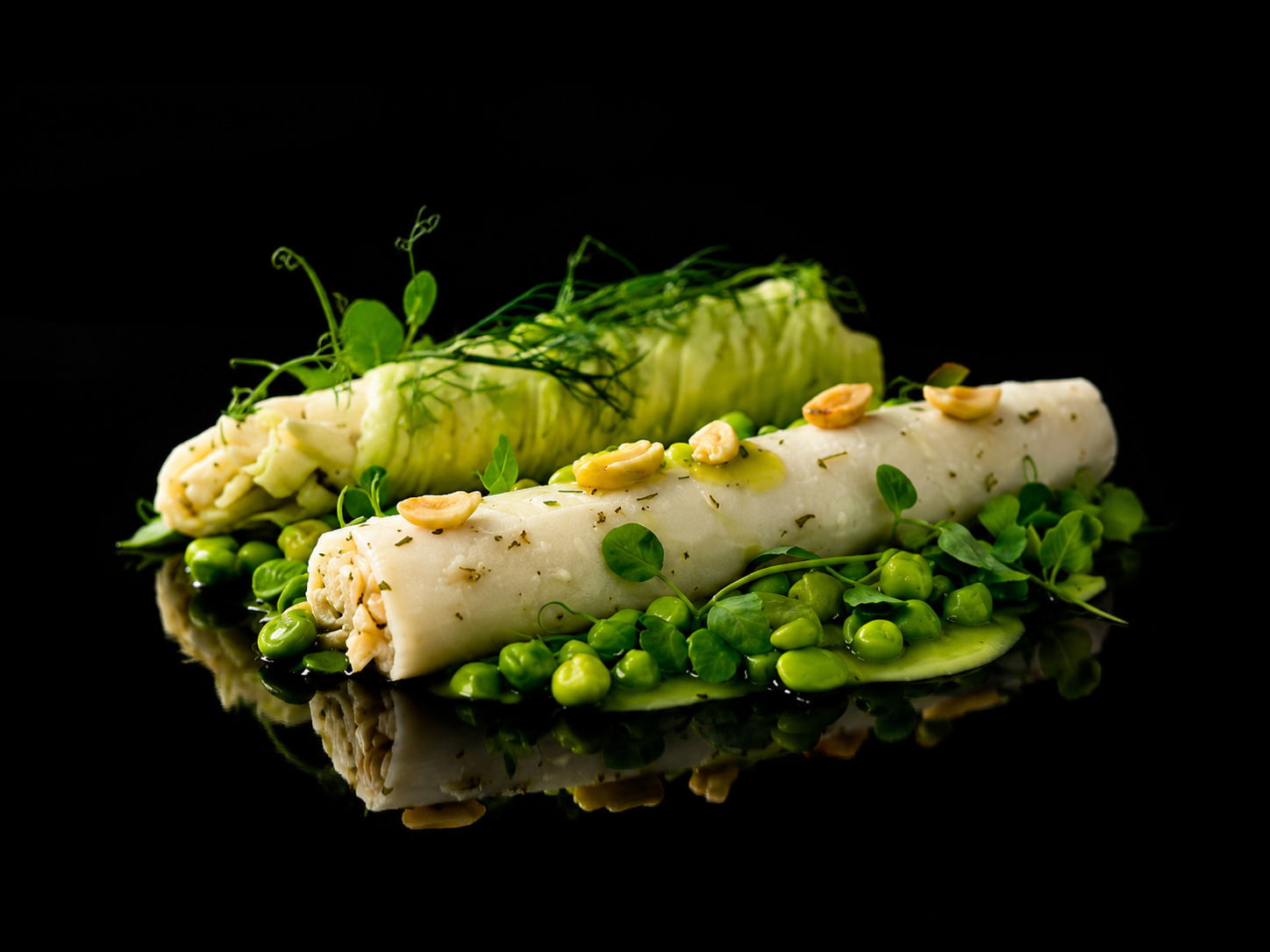 Rouleau de fromage blanc décoré de pois verts, noix et herbes, placé sur un lit de pois verts et de jeunes pousses, avec de la roquette en haut, sur un fond noir