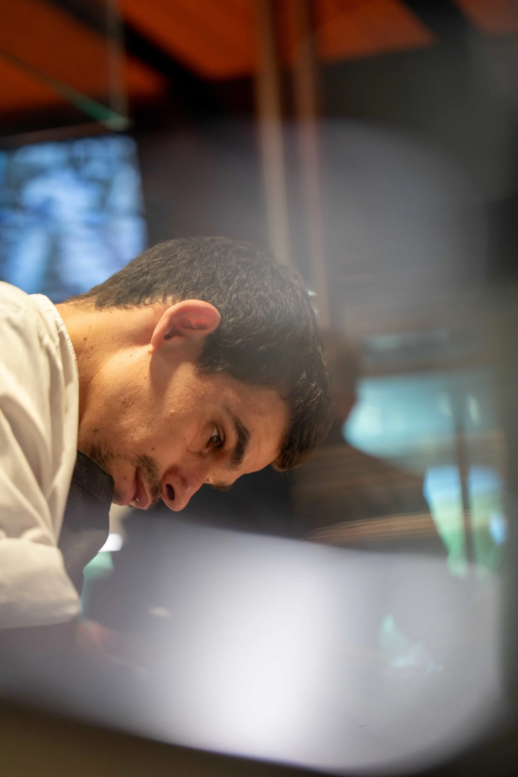 Un homme avec les yeux fixés sur une surface, dans un intérieur avec des éléments en bois et des fenêtres en arrière-plan.