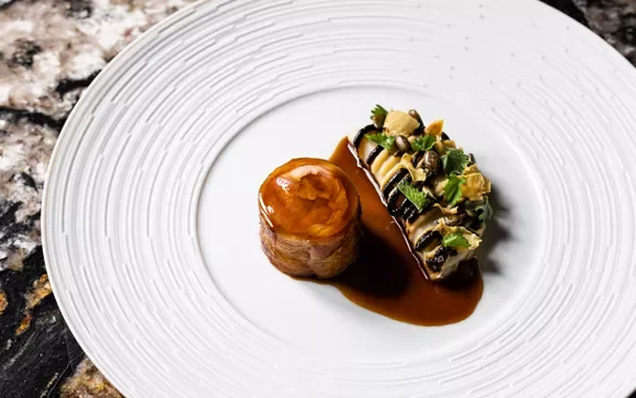 Presentation d'un plat avec un nem et une tranche de viande en sauce sur une assiette blanche.