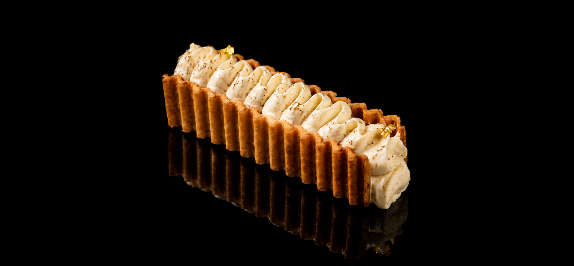 Dessert avec une base rectangulaire en biscuits, double couche, garnie de crème fouettée décorée de petits feuillets d'or, sur fond noir.