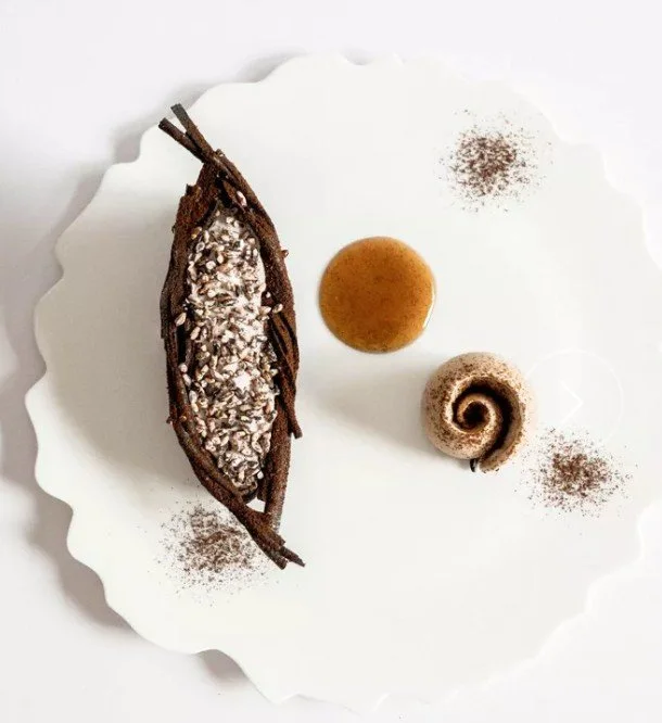 Assiette avec un dessert à base de chocolat, garniture de graines de chia, une sauce caramélisée, une spirale de biscuit, et des poudres de cacao.