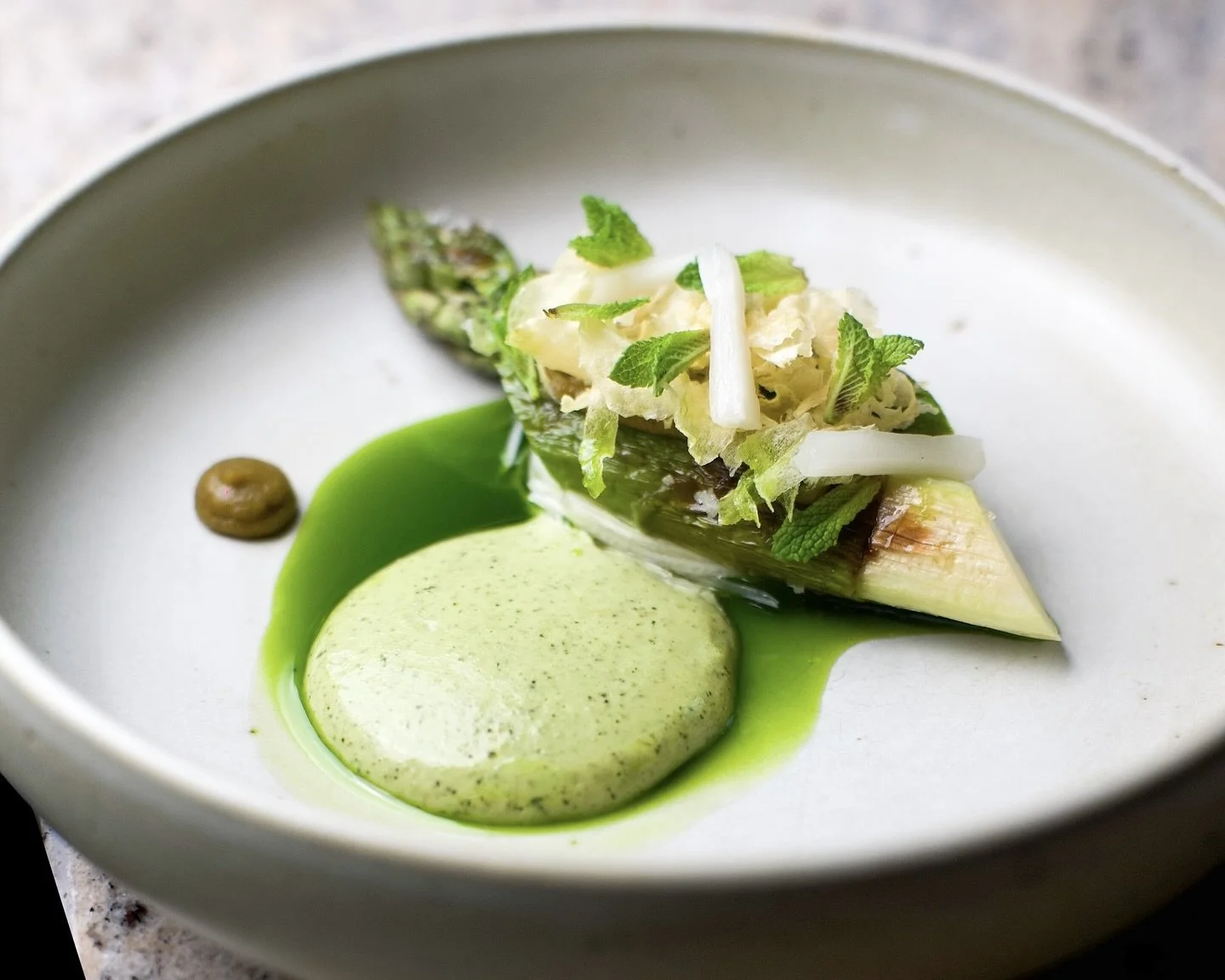 Assiette avec un asperge grillée garnie de purée verte, sauce verte, et herbes fraîches.