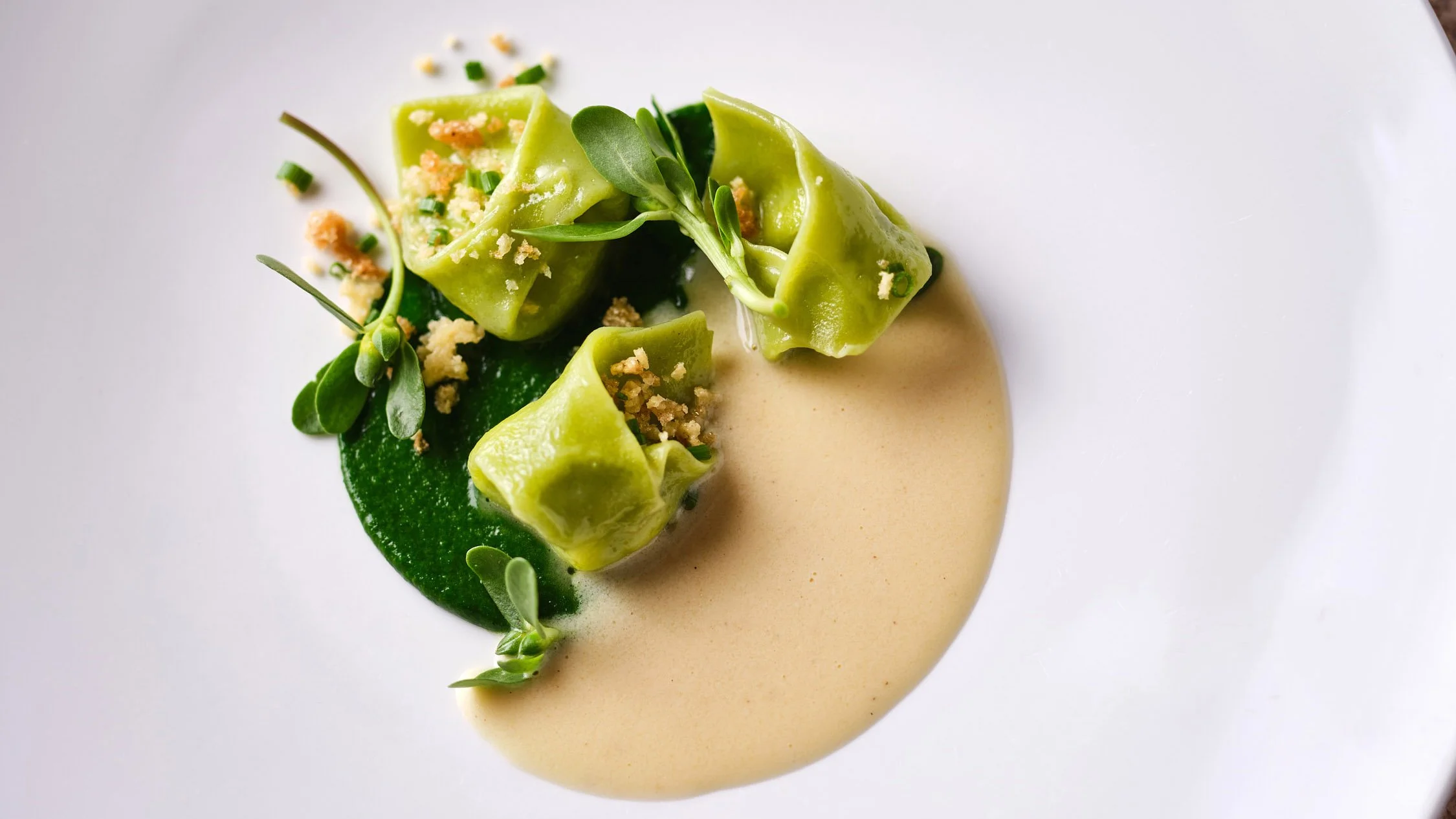 Pâtes vertes garnies de microverts, accompagné d'une sauce beige, sur une assiette blanche.