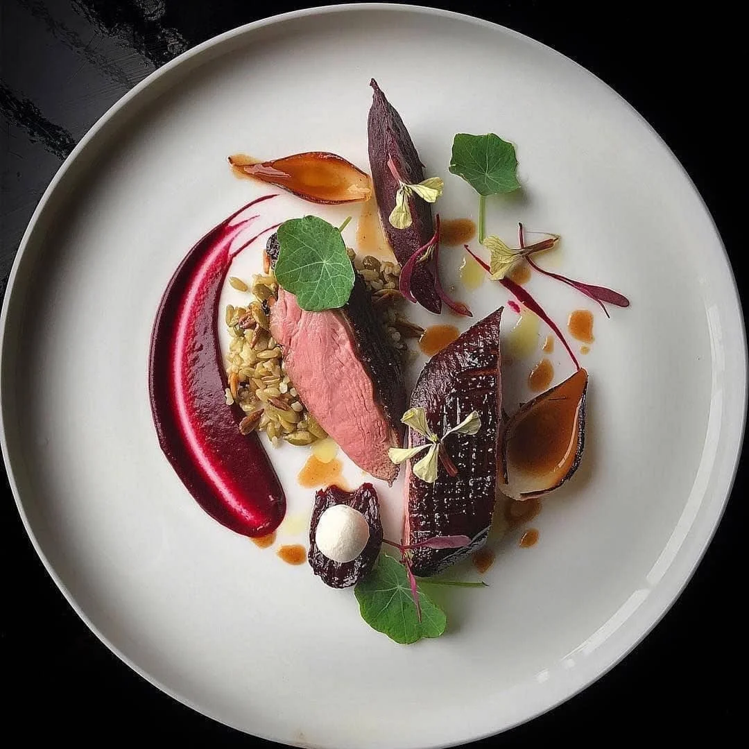 Assiette gastronomique avec de la viande rouge, des légumes racines, des micro-pousses et des sauces artistiques.