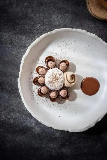 Soucoupe de chocolat et de crème avec plusieurs petits rouleaux de chocolat et une boule de chocolat sur une assiette blanche.