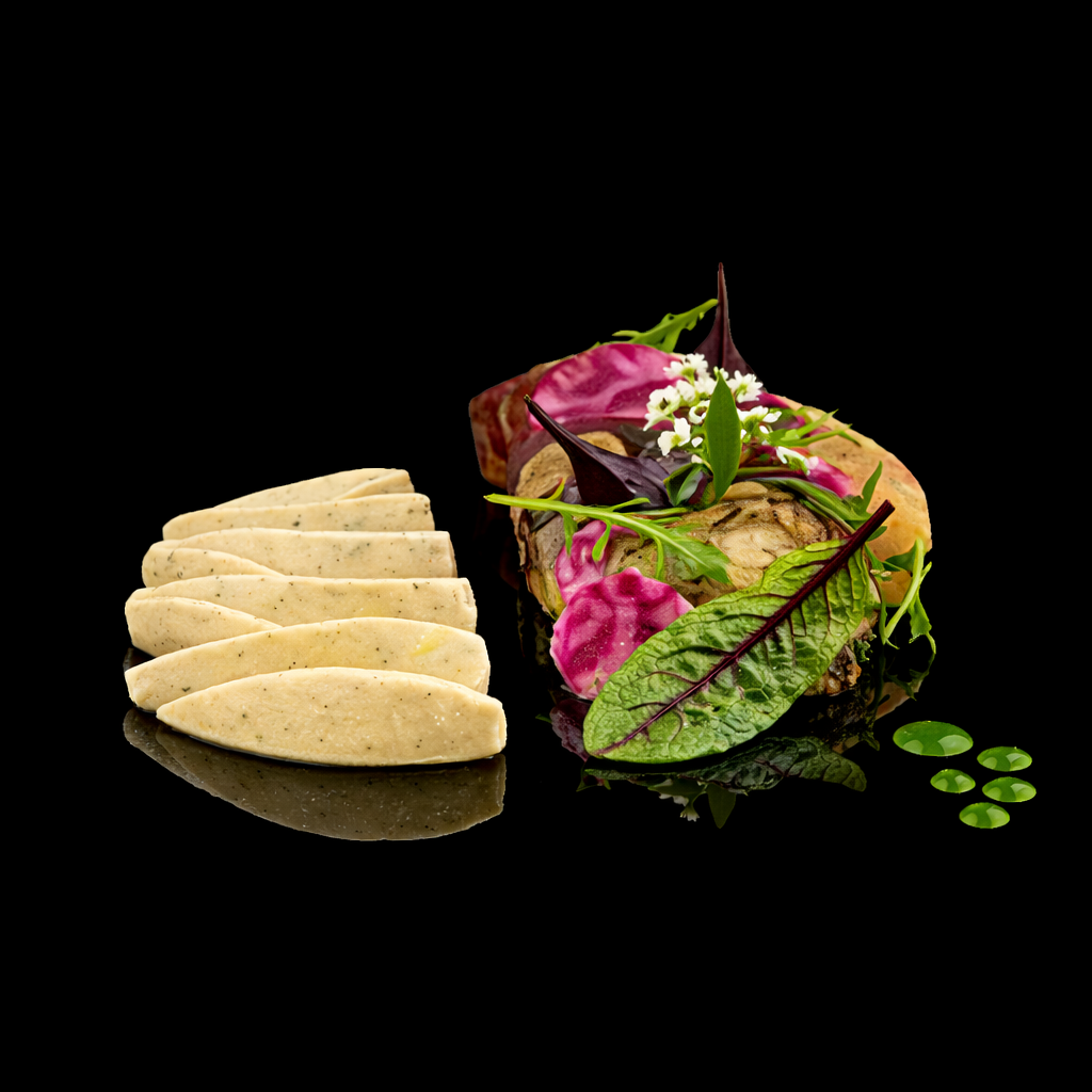 Assiette de terrine de poisson ou de viande, accompagnée de feuilles de salade et de purée de pommes de terre, décorée de fleurs comestibles et de gouttes de sauce verte, sur fond noir.