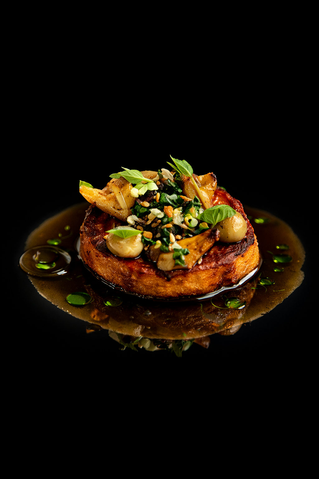 Un plat gastronomique avec une tranche de viande, garniture de légumes, herbes fraîches, et une sauce sur fond noir.
