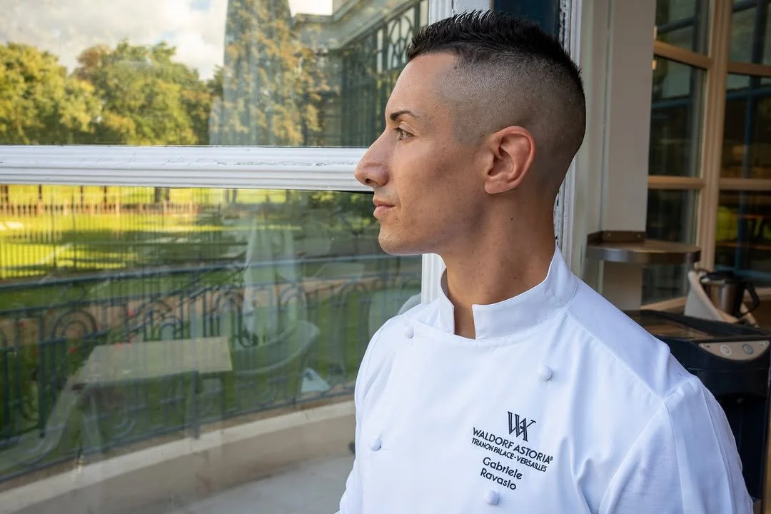 Un chef en uniforme blanc regarde par une fenêtre lors d'une journée ensoleillée.