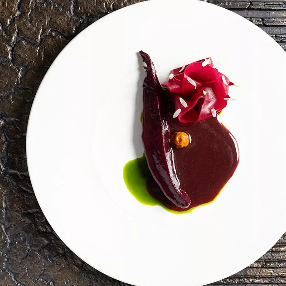 Assiette élégante avec un plat de viande ou légume en sauce rouge, garnie d'une sauce verte, accompagnée d'une garniture rose