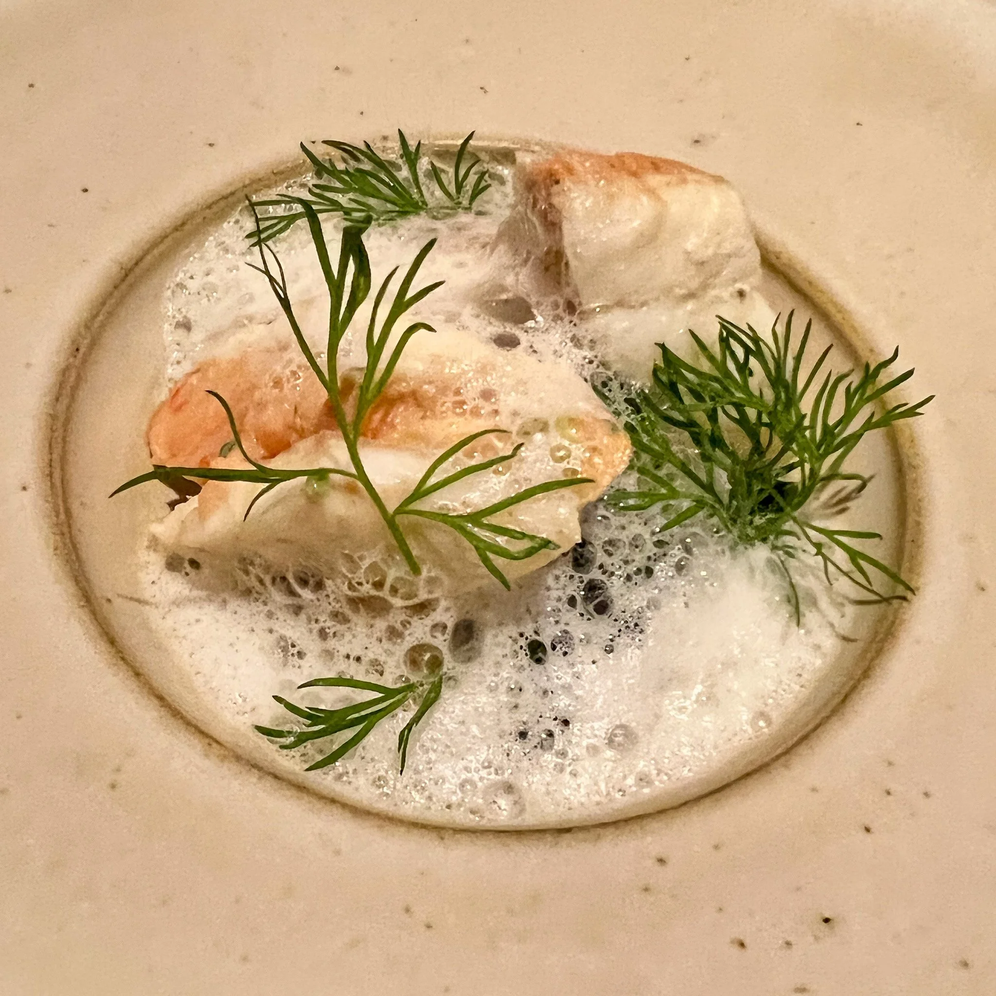 Crème à la surface, garnie de morceaux de poisson, de fines herbes et de mousse