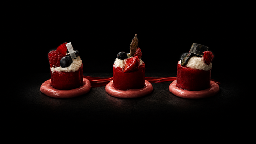 Trois mini gâteaux avec des fruits rouges et des décorations en chocolat, sur une surface noire.