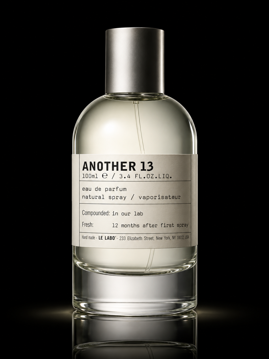 Une bouteille de parfum transparent avec une étiquette blanche portant le nom 'Another 13', contenant un liquide clair, et un bouchon argenté, avec un fond noir.
