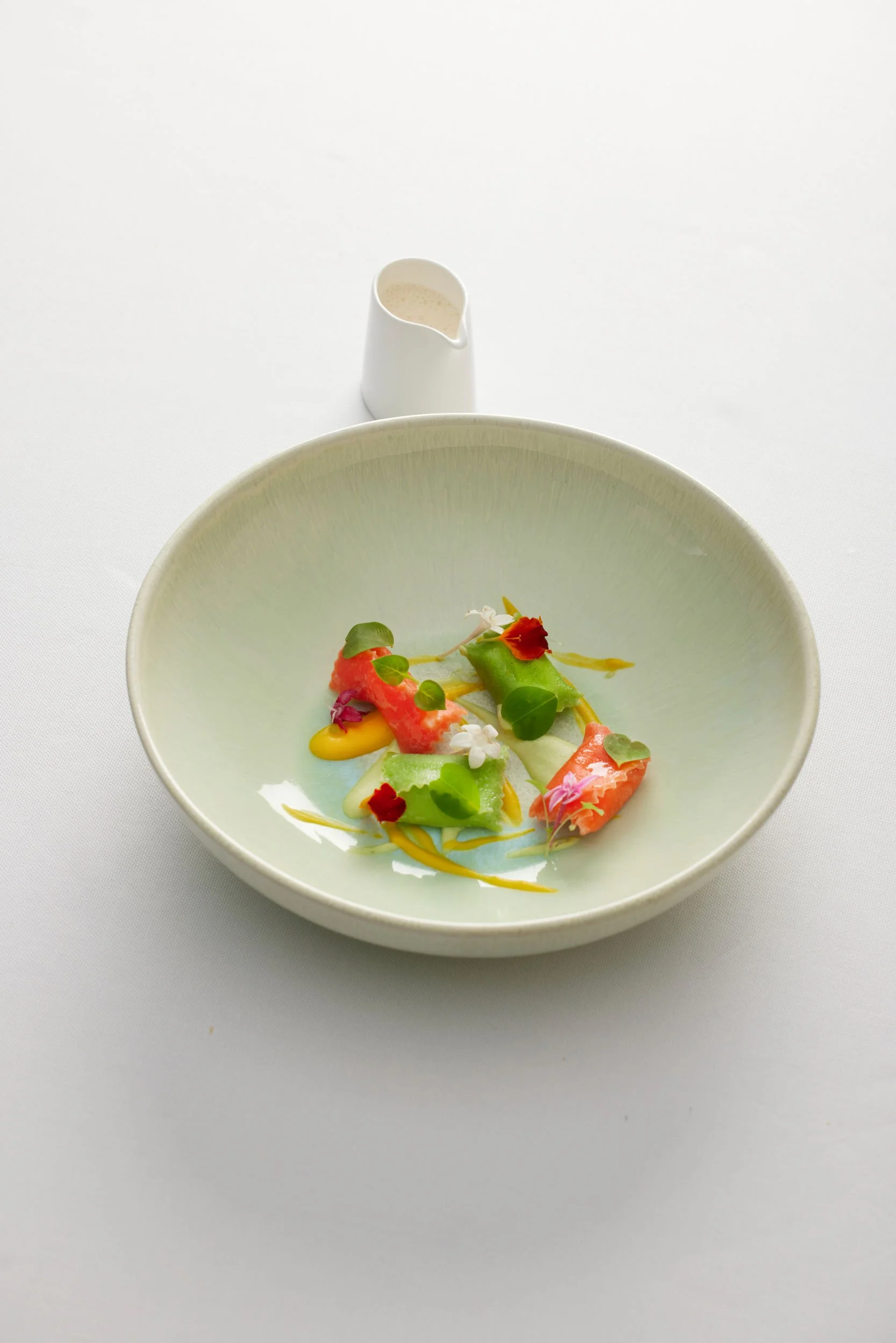 Une assiette de viande, légumes et fleurs comestibles, avec une petite cruche de sauce à côté