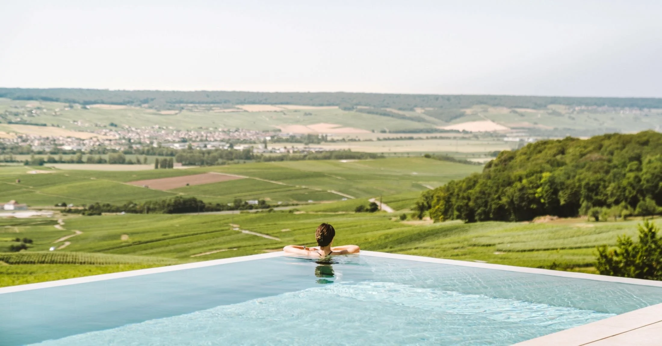 Personne nageant dans une piscine avec une vue sur la campagne verte et les collines environnantes.
