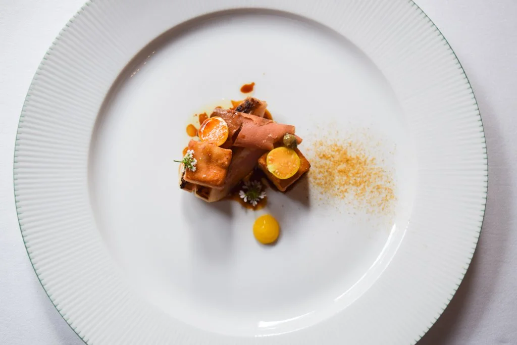 Assiette de nourriture gastronomique avec petits morceaux de viande, légumes et sauce, présentée de manière artistique.