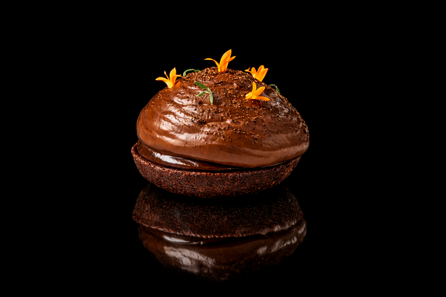 Dessert au chocolat décoré de fleurs et de feuilles, présenté sur un fond noir