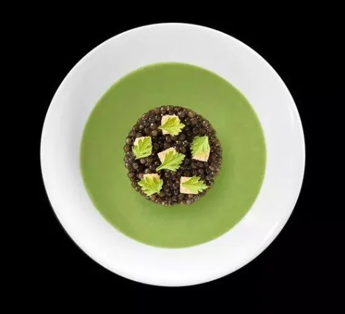 Assiette avec un crumble de mûres sur une cuillère de gelée verte, garnie de feuilles de menthe.