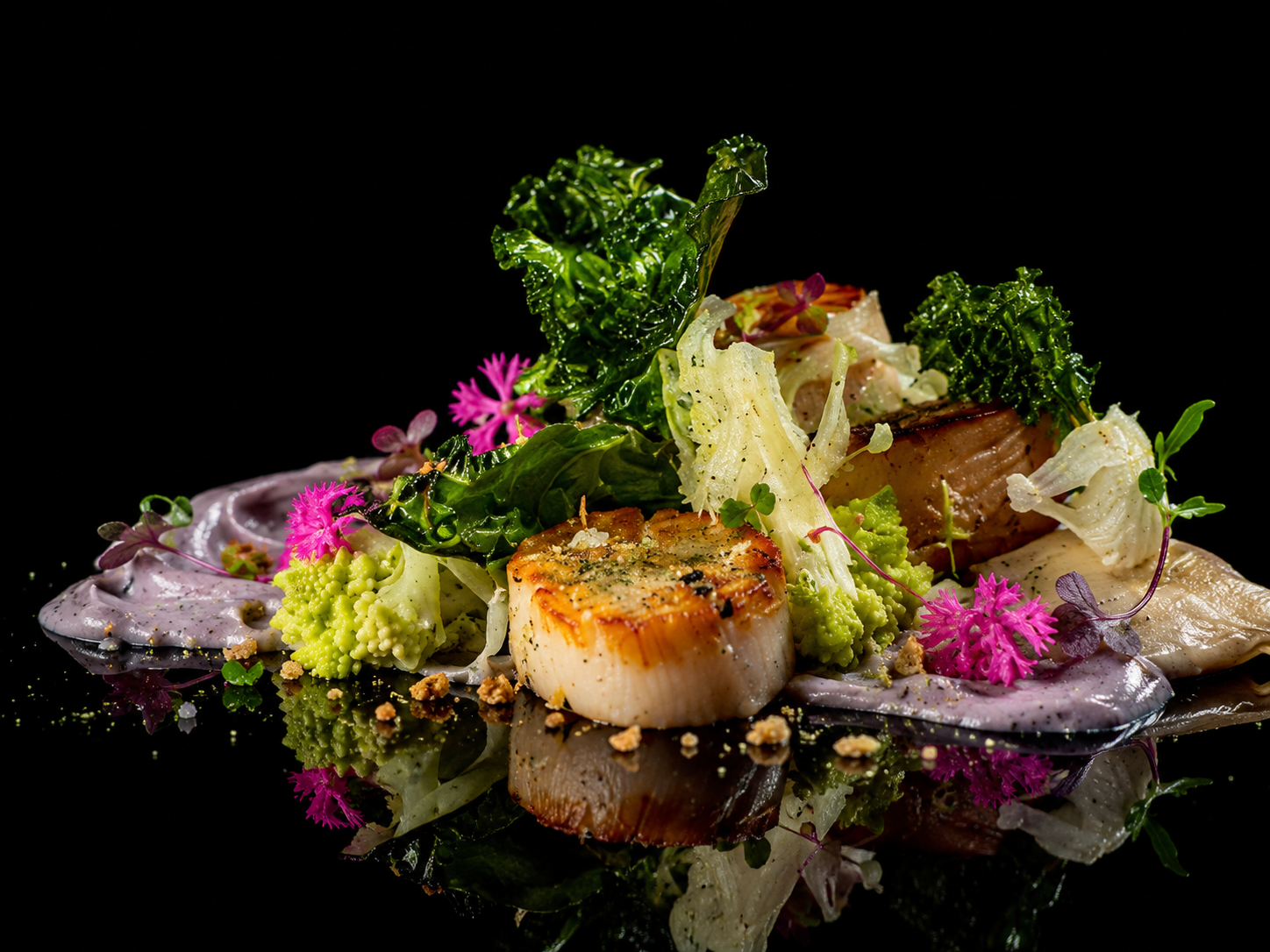 Assiette de ssaté de poisson avec légumes verts, fleurs comestibles et mousse violette, décorée avec des herbes fraîches et des épices, sur fond noir.