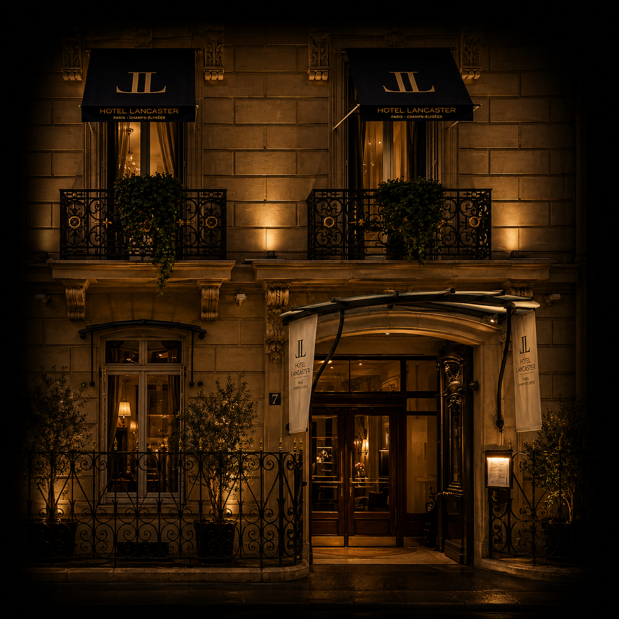 Façade illuminée de l'hôtel Lancaster à Paris, montrant une entrée principale avec un auvent, des fenêtres avec rideaux, des balcons avec des arbustes et des enseignes lumineuses.