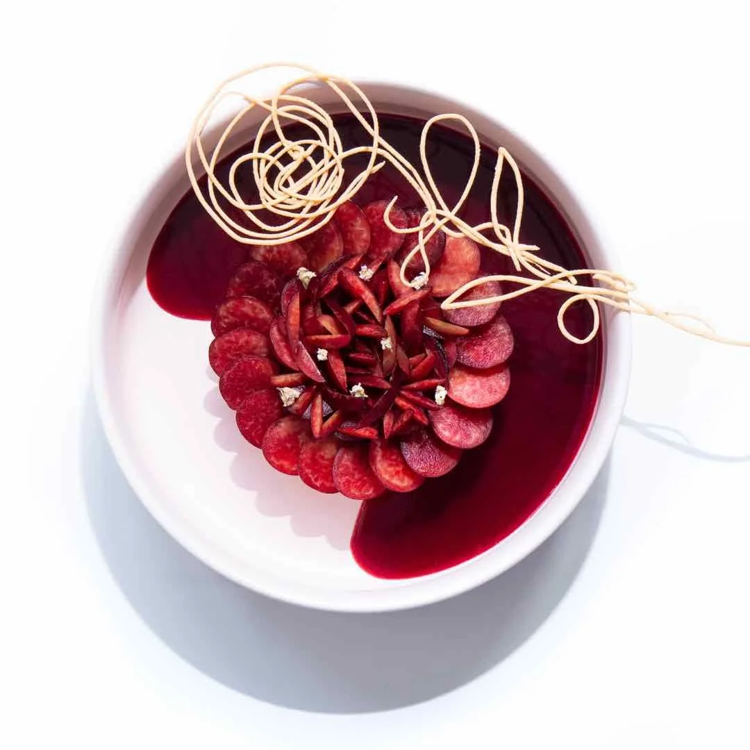 Dessert à base de framboises, avec décoration en filaments de chocolat blanc ou pâte d'amande, dans un bol blanc avec sauce rouge