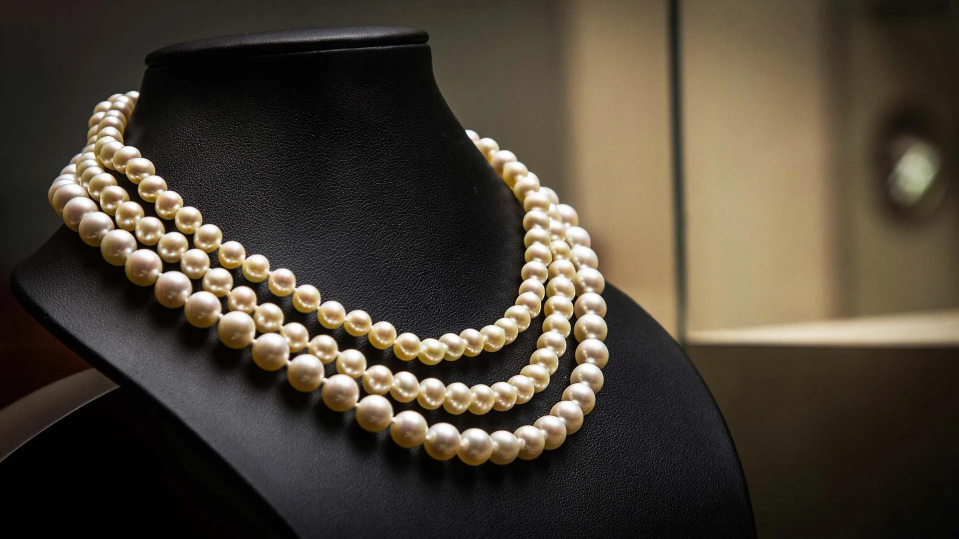Colliers de perles blanches sur un support noir dans une vitrine de musée